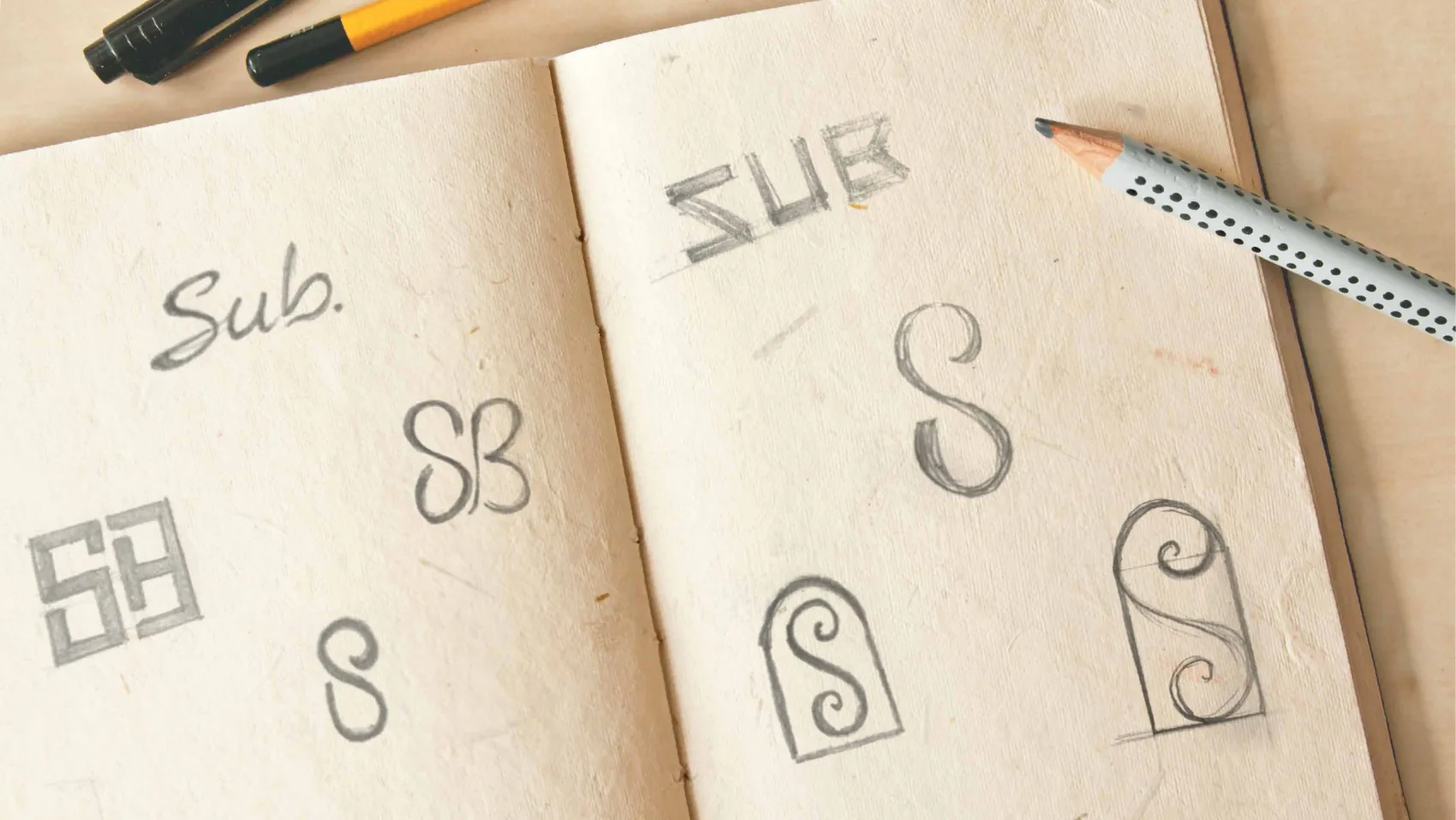 Pencil sketches in a notebook exploring SUB monogram routes — SB ligatures, framed marks and an S inside an arch