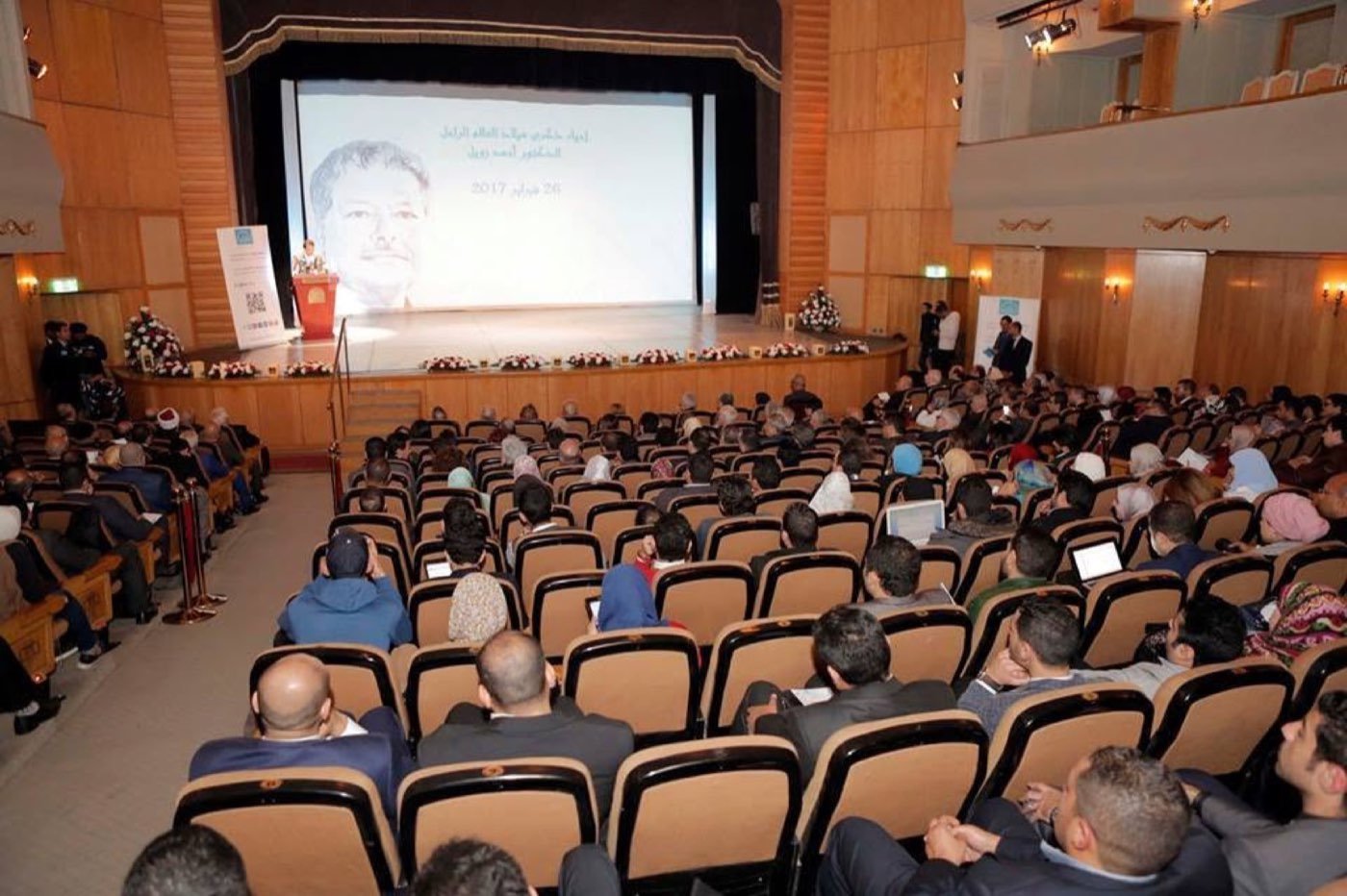 A packed auditorium at Zewail City, Dr. Ahmed Zewail's portrait on the screen for the 26 February 2017 commemoration